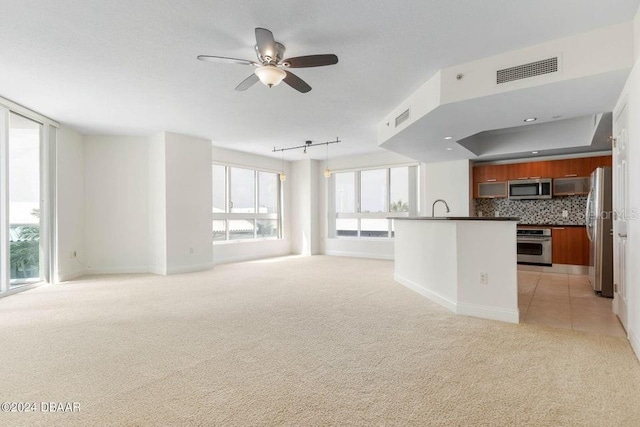 unfurnished living room featuring rail lighting, light colored carpet, ceiling fan, and sink