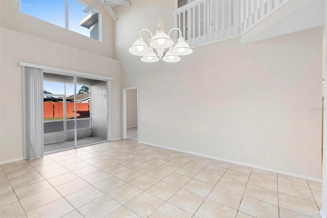 tiled empty room with plenty of natural light, ceiling fan with notable chandelier, and a high ceiling