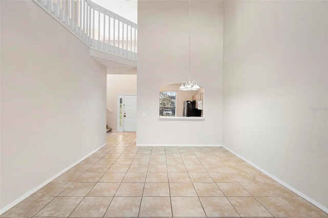 unfurnished living room with light tile patterned floors, a chandelier, and a towering ceiling