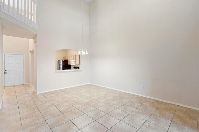 empty room with light tile patterned flooring, a high ceiling, and a chandelier