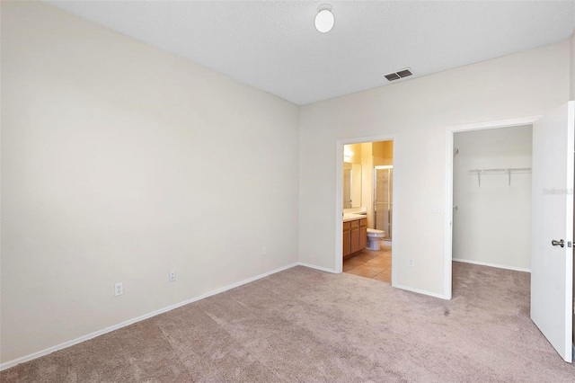 unfurnished bedroom with a spacious closet, connected bathroom, a closet, light colored carpet, and a textured ceiling