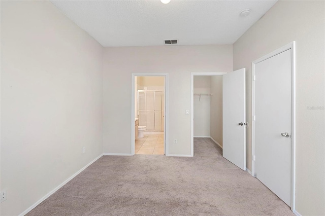 unfurnished bedroom with ensuite bath, a walk in closet, light carpet, and a closet