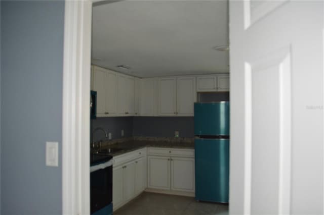 kitchen featuring refrigerator, sink, light tile patterned floors, white cabinets, and range