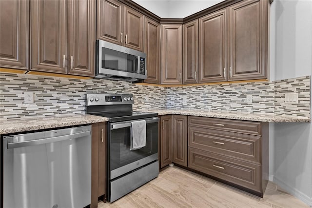 kitchen with light stone countertops, appliances with stainless steel finishes, dark brown cabinets, and backsplash