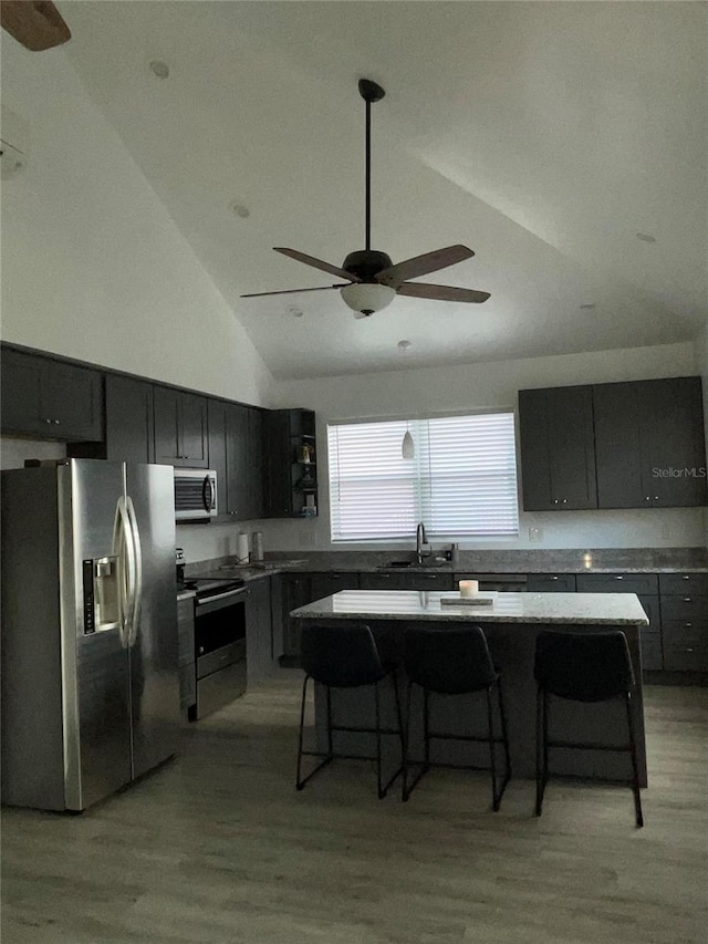 kitchen featuring a breakfast bar, stainless steel appliances, high vaulted ceiling, light hardwood / wood-style floors, and a kitchen island