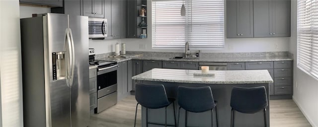 kitchen with sink, stainless steel appliances, light stone counters, gray cabinets, and a kitchen island