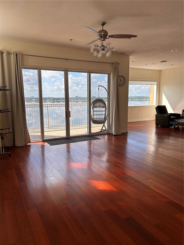 spare room featuring a textured ceiling, a water view, ceiling fan, and dark wood-type flooring