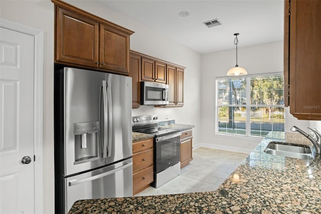 kitchen with hanging light fixtures, sink, dark stone countertops, appliances with stainless steel finishes, and light tile patterned flooring