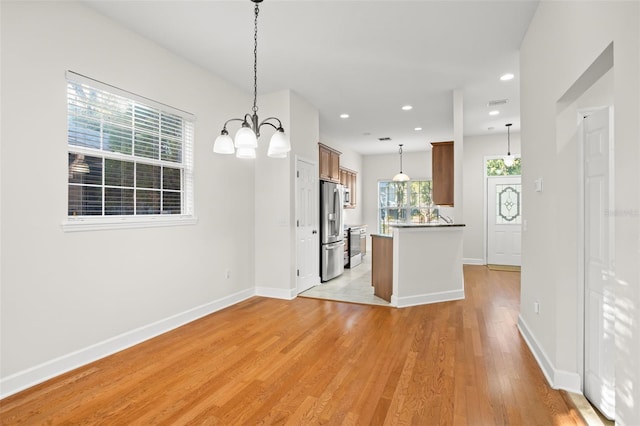 kitchen featuring hanging light fixtures, stainless steel appliances, an inviting chandelier, kitchen peninsula, and light hardwood / wood-style floors