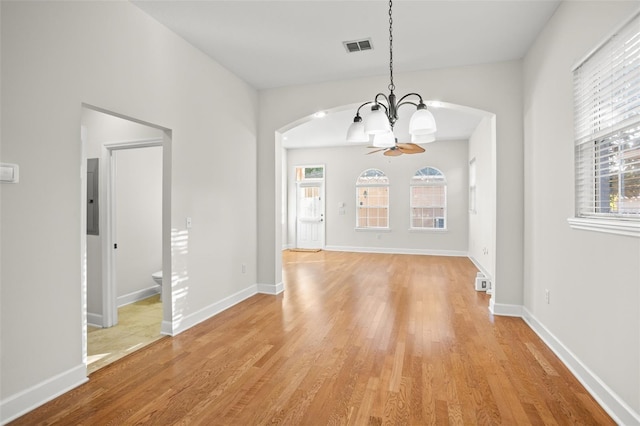 unfurnished dining area with ceiling fan with notable chandelier, electric panel, light hardwood / wood-style flooring, and a wealth of natural light