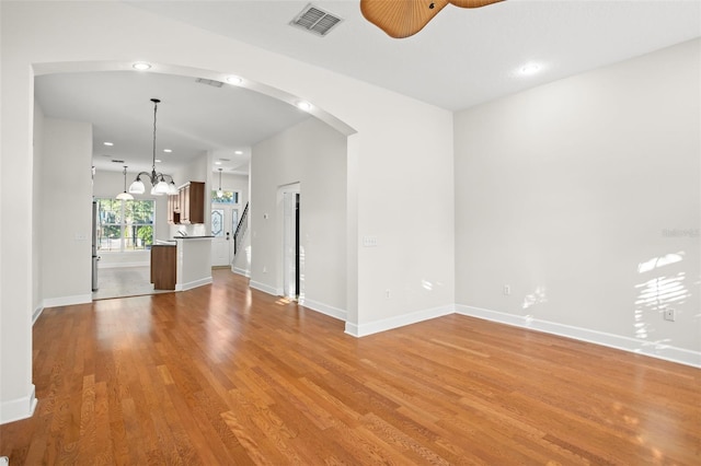 unfurnished living room featuring ceiling fan with notable chandelier and light wood-type flooring