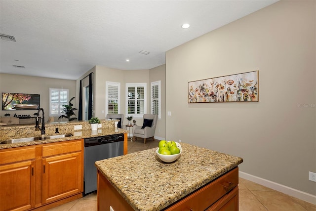 kitchen featuring light stone counters, stainless steel dishwasher, sink, light tile patterned floors, and a kitchen island