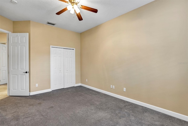 unfurnished bedroom featuring dark colored carpet, a closet, and ceiling fan