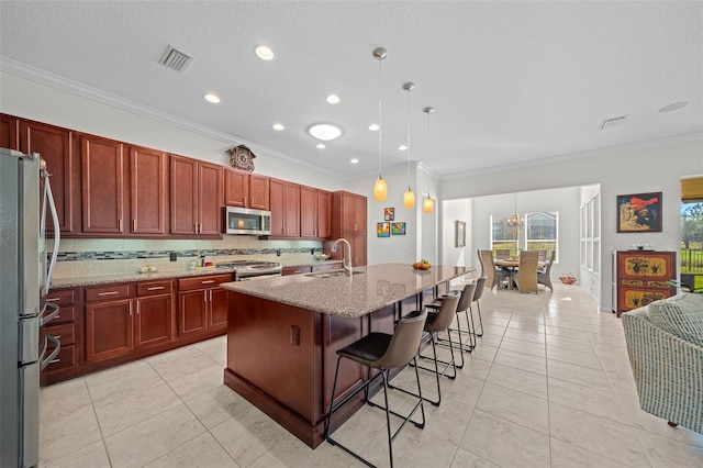 kitchen featuring a center island with sink, light stone countertops, ornamental molding, decorative light fixtures, and stainless steel appliances