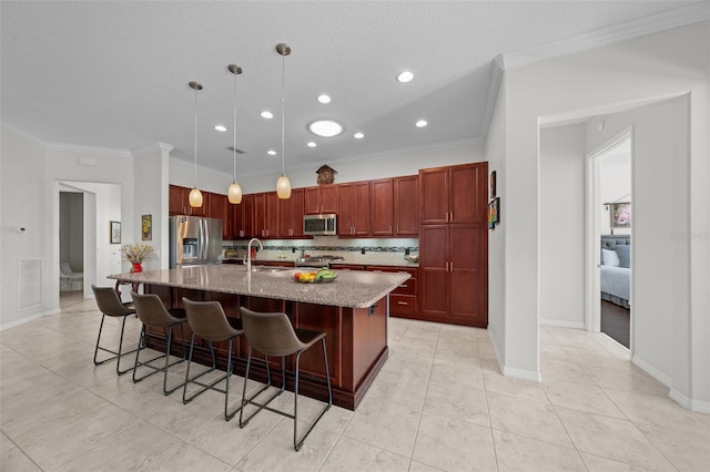 kitchen with a kitchen breakfast bar, an island with sink, decorative light fixtures, appliances with stainless steel finishes, and ornamental molding