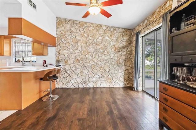 kitchen with ceiling fan, lofted ceiling, dark hardwood / wood-style floors, and a breakfast bar area