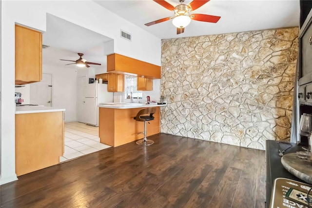 kitchen with light tile patterned flooring, a breakfast bar area, white refrigerator, ceiling fan, and kitchen peninsula