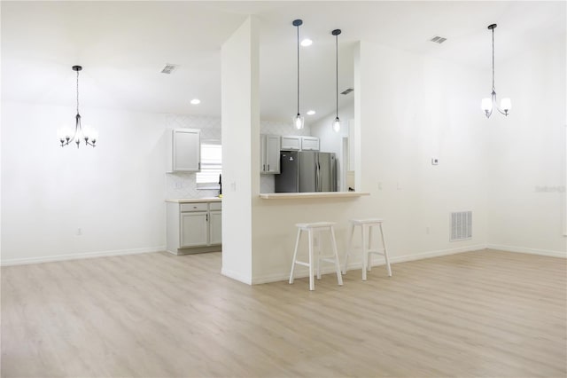 kitchen with stainless steel fridge, light wood-type flooring, a chandelier, and pendant lighting