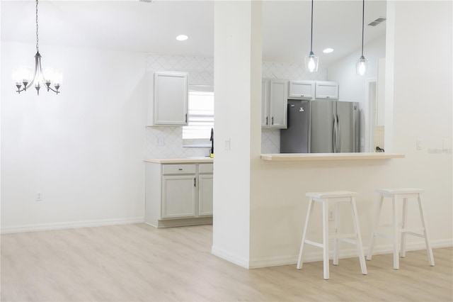 kitchen with light hardwood / wood-style flooring, pendant lighting, stainless steel fridge, an inviting chandelier, and white cabinets