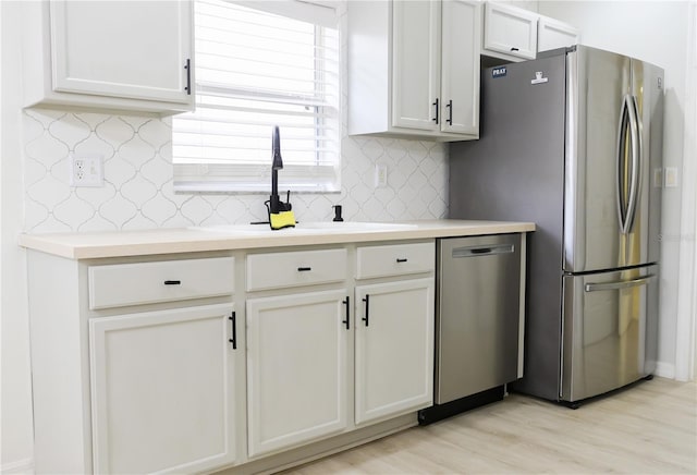 kitchen with sink, white cabinetry, light hardwood / wood-style flooring, decorative backsplash, and appliances with stainless steel finishes