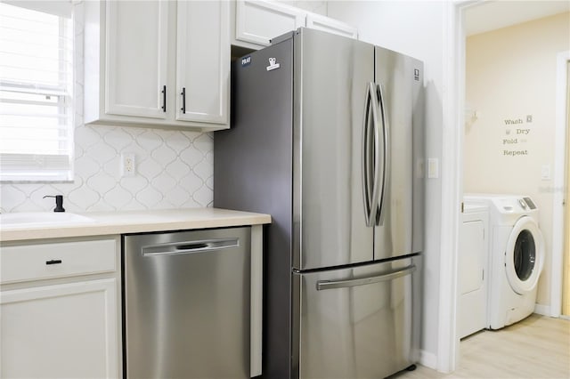 kitchen featuring washer and clothes dryer, stainless steel appliances, light hardwood / wood-style floors, white cabinets, and sink