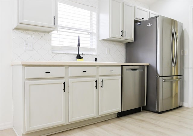 kitchen with appliances with stainless steel finishes, tasteful backsplash, white cabinetry, and light hardwood / wood-style floors