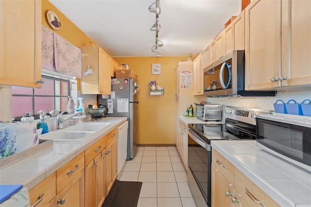 kitchen featuring tile countertops, appliances with stainless steel finishes, a sink, and decorative backsplash