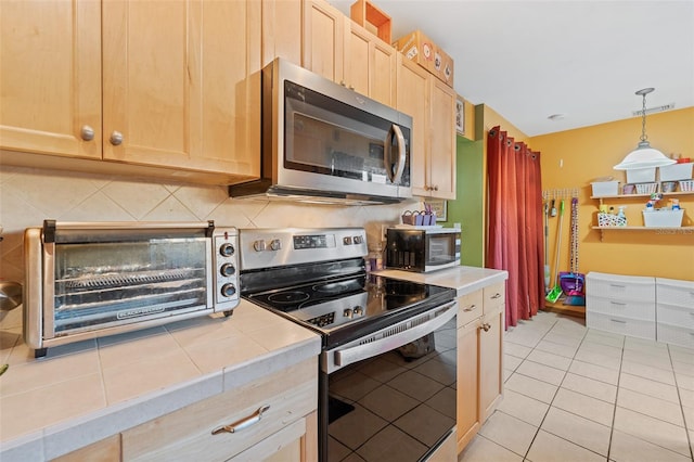 kitchen with tile countertops, stainless steel appliances, tasteful backsplash, hanging light fixtures, and light brown cabinetry