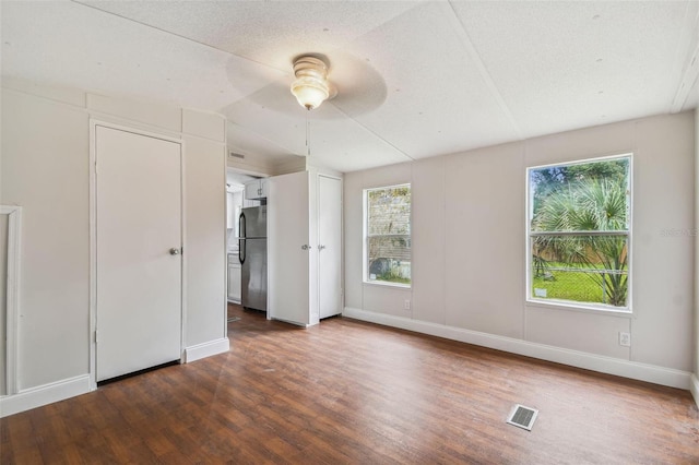 unfurnished bedroom with multiple windows, dark hardwood / wood-style flooring, stainless steel refrigerator, and ceiling fan