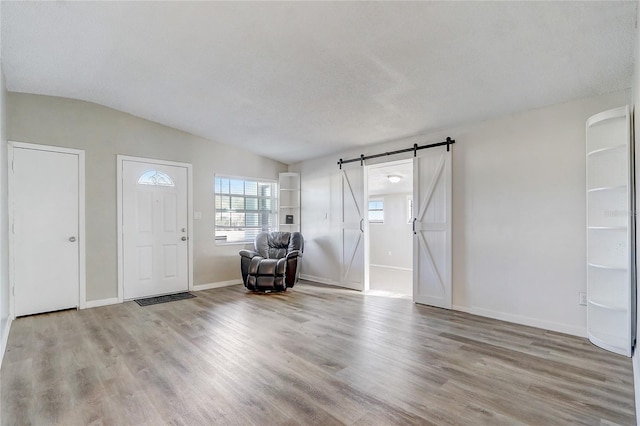 entrance foyer with a textured ceiling, a barn door, light hardwood / wood-style flooring, and vaulted ceiling