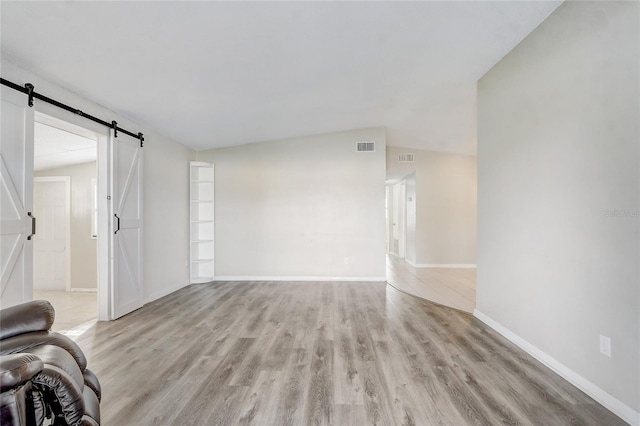 unfurnished living room featuring lofted ceiling, a barn door, and light wood-type flooring