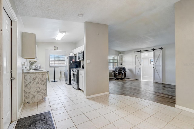 kitchen featuring a textured ceiling, stainless steel appliances, sink, a barn door, and light tile patterned flooring