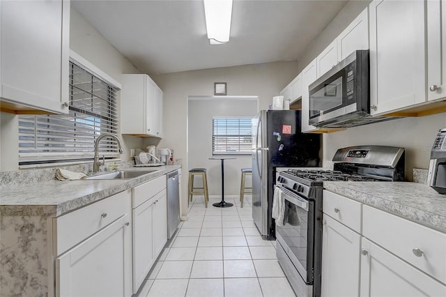 kitchen featuring stainless steel appliances, sink, light tile patterned floors, white cabinetry, and lofted ceiling