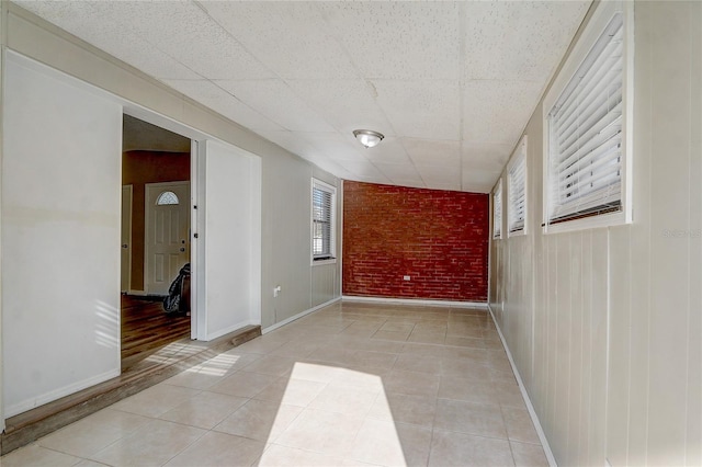 tiled spare room with a paneled ceiling and brick wall