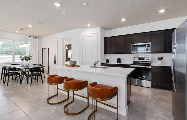 kitchen with a kitchen island with sink, sink, hanging light fixtures, a breakfast bar area, and stainless steel appliances