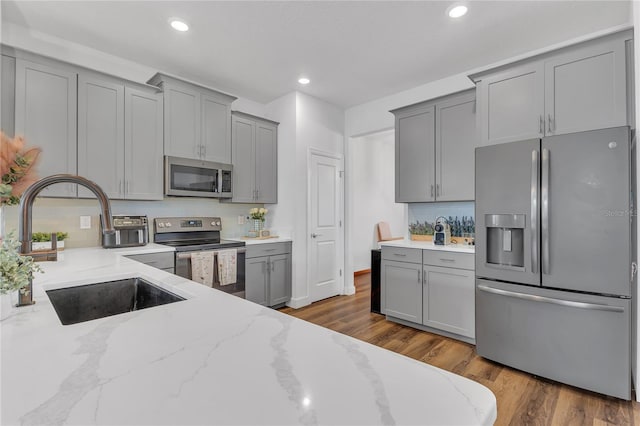 kitchen featuring sink, stainless steel appliances, light stone counters, dark hardwood / wood-style flooring, and backsplash