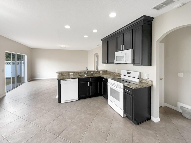 kitchen with sink, kitchen peninsula, dark stone countertops, white appliances, and light tile patterned floors