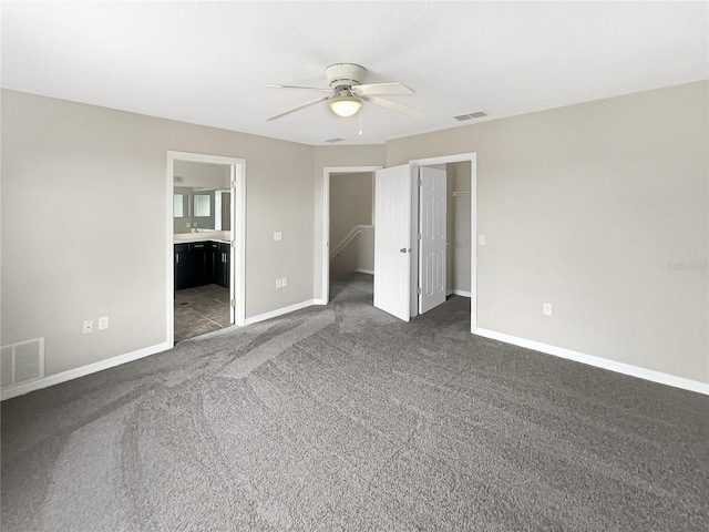 unfurnished bedroom with dark carpet, ensuite bathroom, a walk in closet, ceiling fan, and a closet