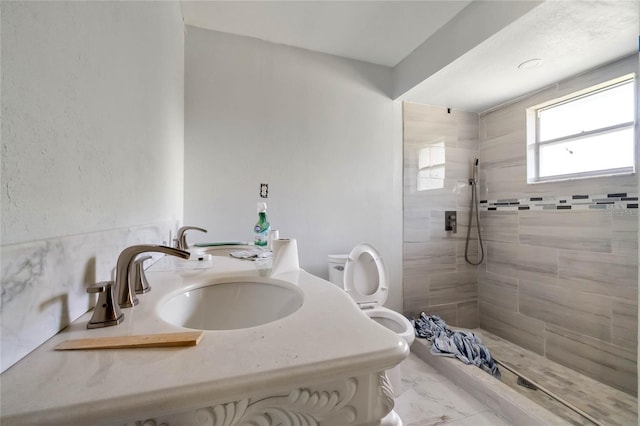 bathroom with a tile shower, toilet, and sink