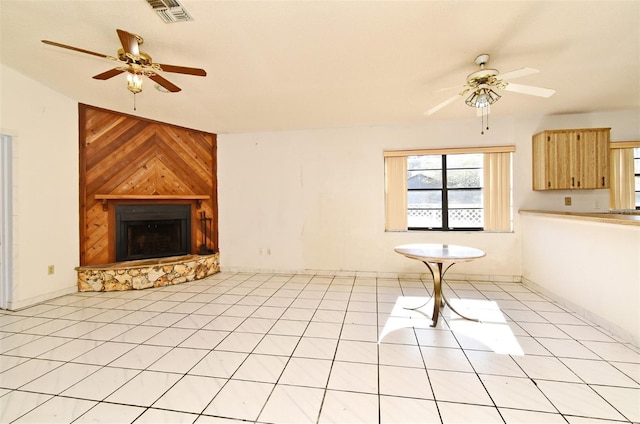 unfurnished living room featuring ceiling fan, wood walls, light tile patterned flooring, and a fireplace