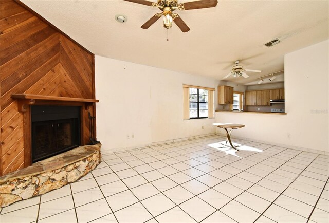 unfurnished living room featuring ceiling fan, a stone fireplace, wood walls, lofted ceiling, and light tile patterned flooring