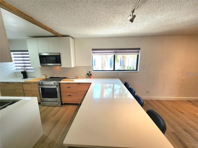 kitchen featuring backsplash, track lighting, light hardwood / wood-style floors, white cabinetry, and stainless steel appliances