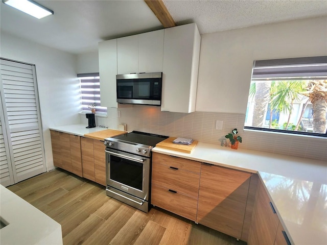 kitchen featuring white cabinets, decorative backsplash, light wood-type flooring, a textured ceiling, and appliances with stainless steel finishes