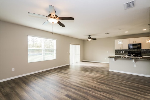 unfurnished living room with ceiling fan with notable chandelier and dark wood-type flooring