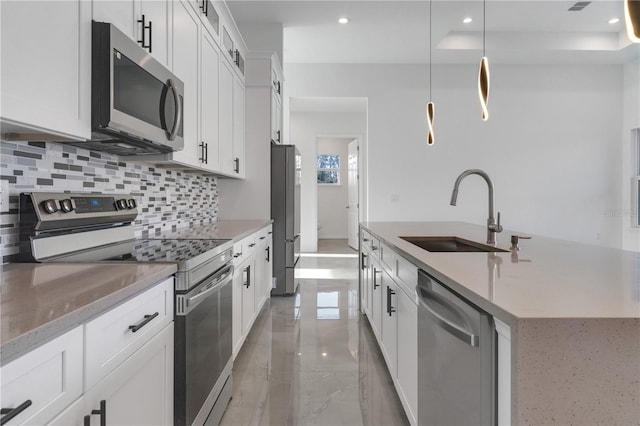 kitchen with sink, stainless steel appliances, an island with sink, pendant lighting, and white cabinets