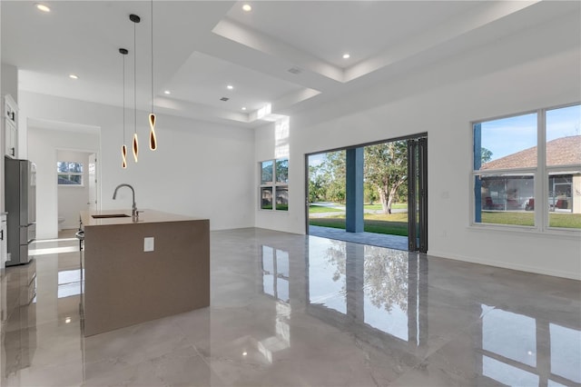 kitchen with stainless steel fridge, a tray ceiling, decorative light fixtures, a center island with sink, and white cabinetry