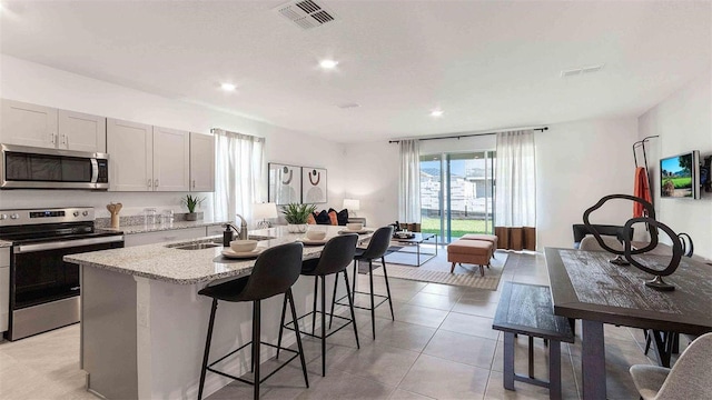 kitchen with sink, stainless steel appliances, a kitchen breakfast bar, light stone counters, and a center island with sink