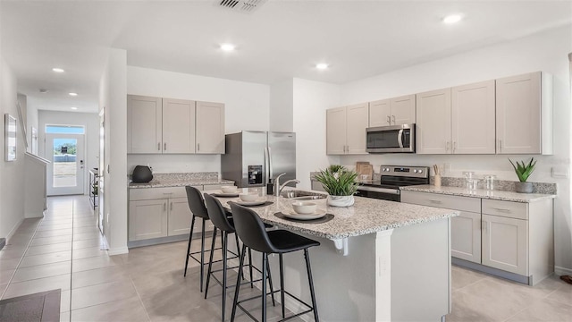 kitchen featuring a center island with sink, a kitchen breakfast bar, sink, light stone countertops, and stainless steel appliances