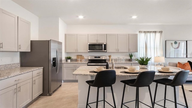 kitchen with sink, light stone counters, an island with sink, a breakfast bar area, and appliances with stainless steel finishes