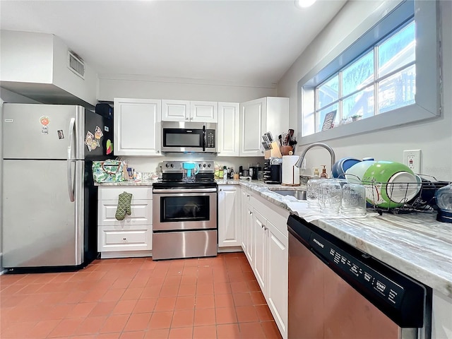 kitchen featuring appliances with stainless steel finishes, light stone counters, sink, white cabinets, and light tile patterned flooring